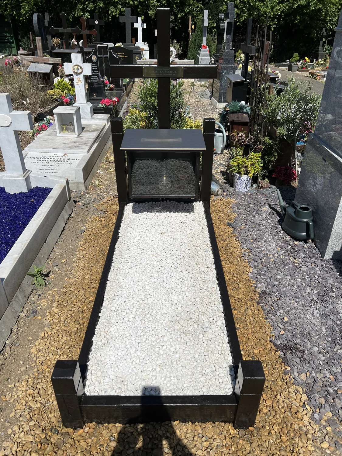 Handmade dark wooden memorial with a cross, glass-fronted cabinet and white stone grave surround